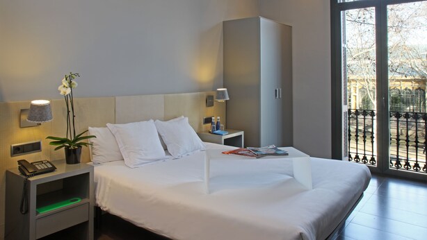 A hotel room with a large bed, a bedside table with a lamp, a phone, and a plant. -  chic&basic Zoo (Barcelona)