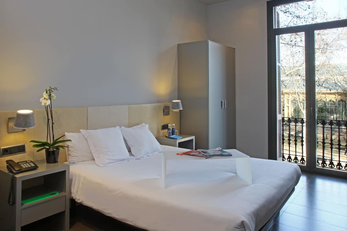 Una habitación de hotel con una cama grande, una mesita de noche con lámpara, un teléfono y una planta.
