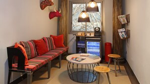 A modern living room with a sofa, a round coffee table, and a small stool. There is a window with curtains and a wall-mounted shelf with magazines. -  chic&basic Zoo (Barcelona)