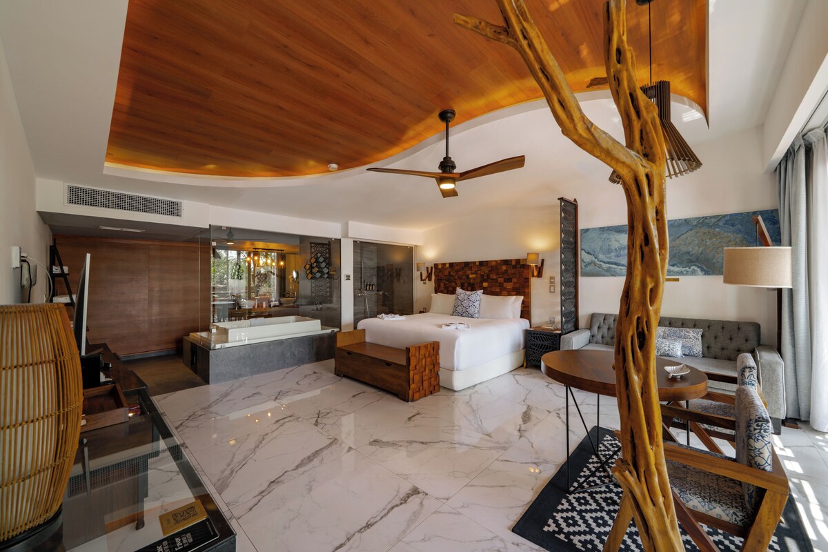 A modern hotel room with a large bed, a sitting area, a bathroom, and a view of the mountains.
