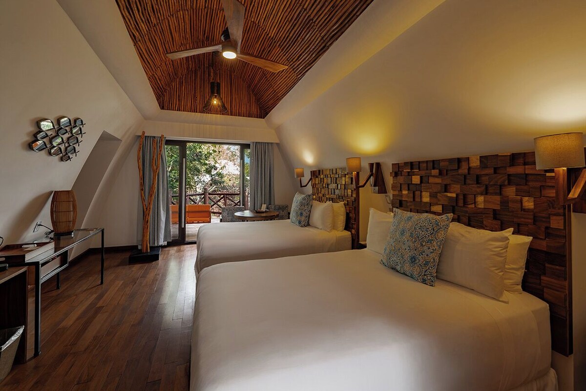 A bedroom with two beds, a wooden ceiling, and a view of the outdoors.