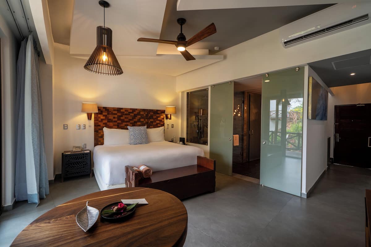 Een moderne hotelkamer met een groot bed, een houten nachtkastje, een plafondventilator en een glazen schuifdeur naar een balkon.