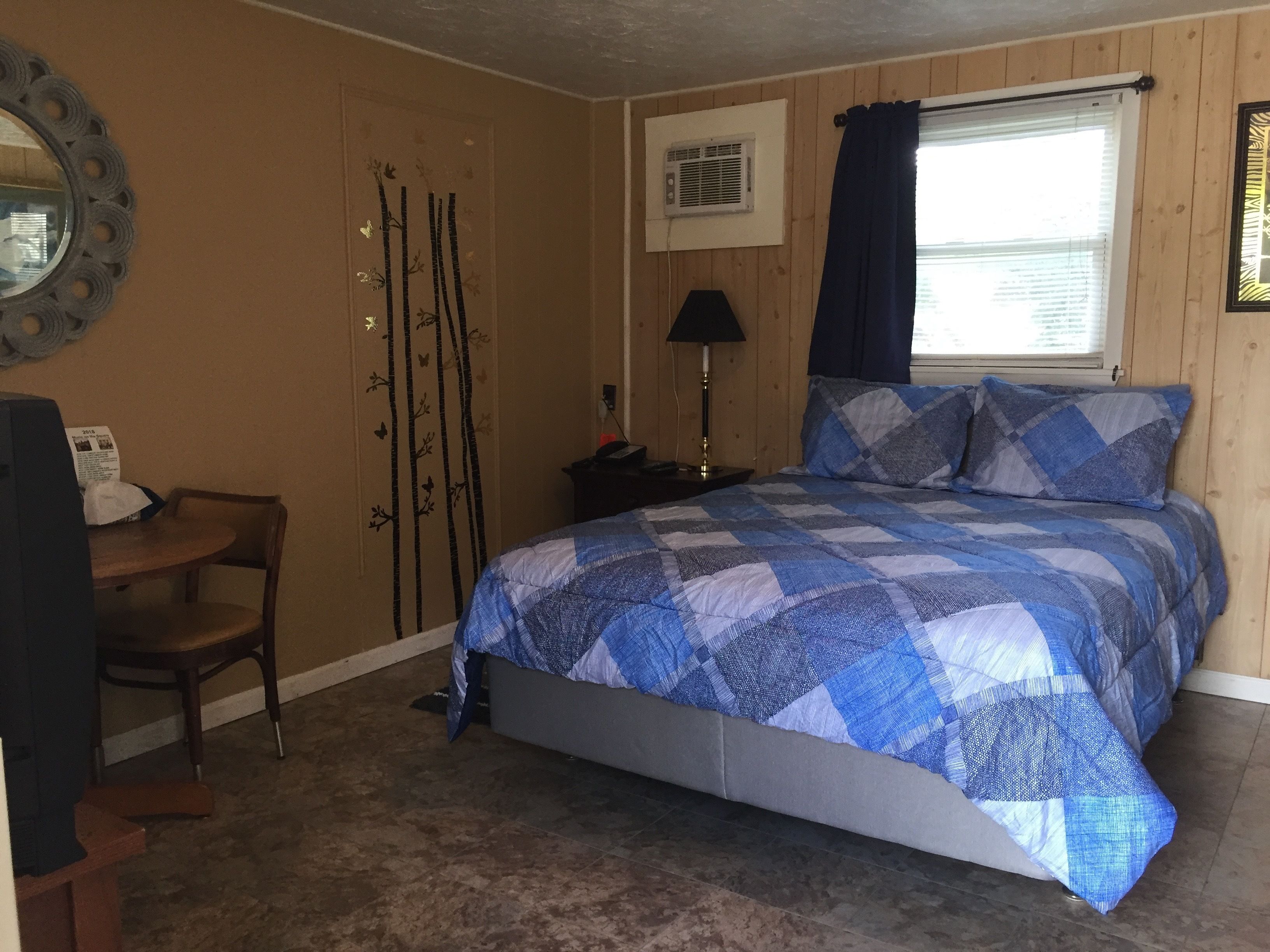 A bedroom with a bed, a chair, a desk, a lamp, and a window with curtains.