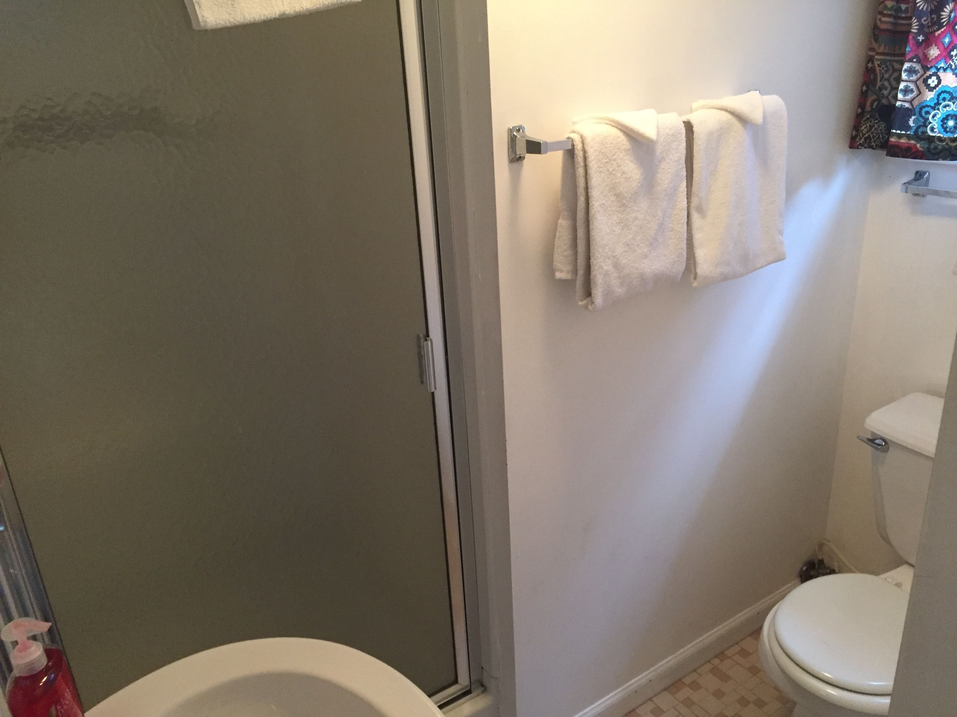 A bathroom with a toilet, a shower, and a towel rack with two towels.