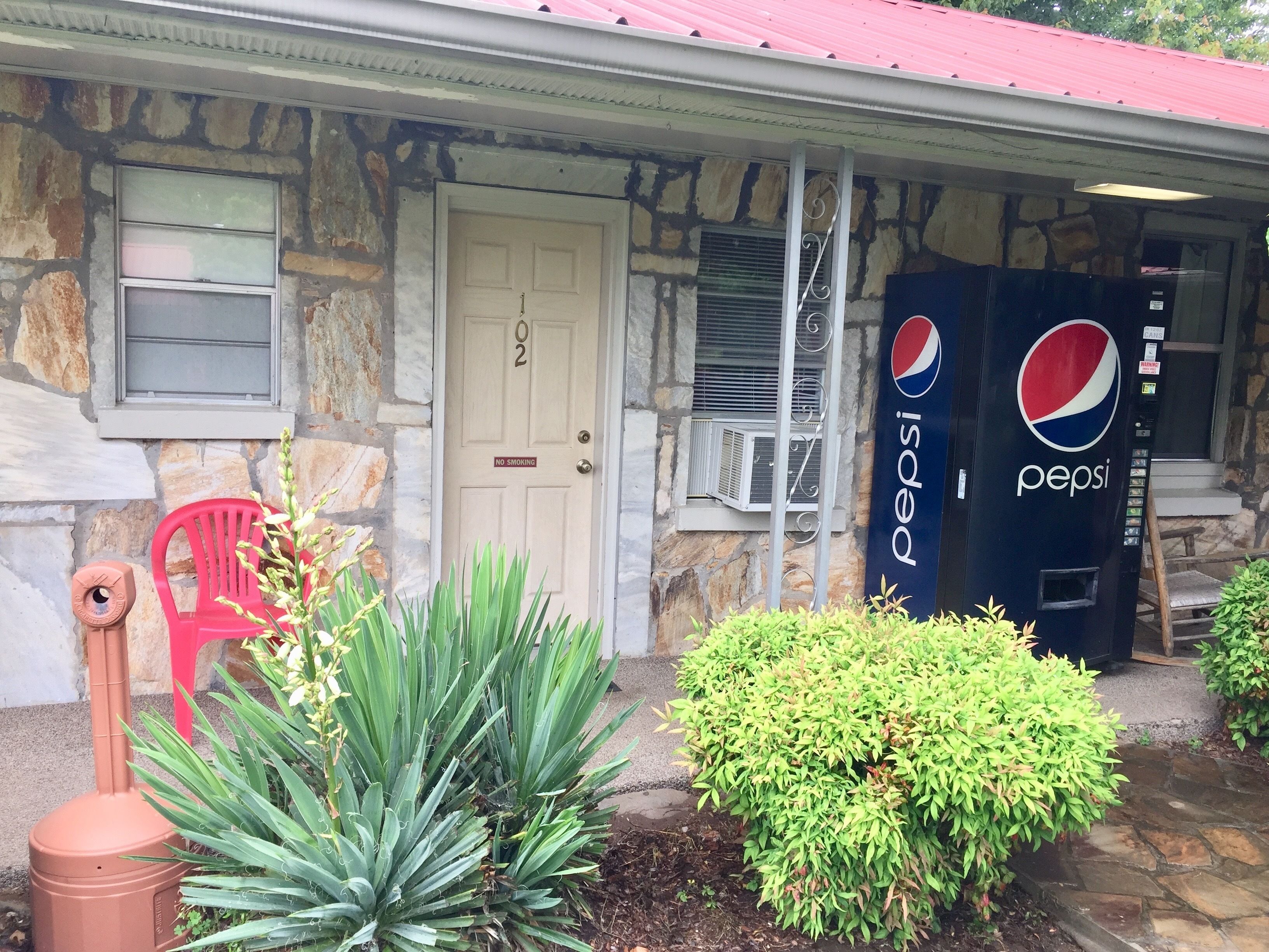 A building with a stone facade, a red roof, a Pepsi vending machine, a red chair, and green plants.