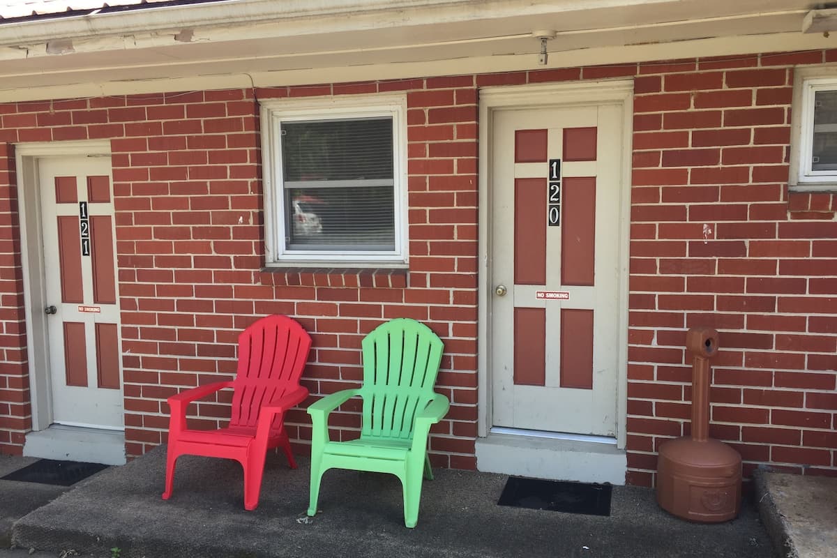 A red brick building with two doors, each marked with a number and a 'No Smoking' sign. Two plastic chairs are placed in front of the doors.