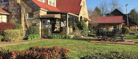 A stone building with a red roof, a covered patio, and a seating area with a table and chairs.