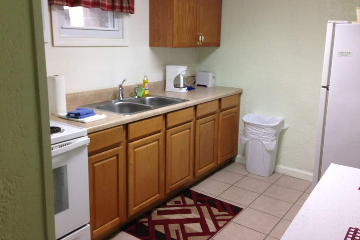 A compact kitchen with wooden cabinets, a double sink, a stove, and a refrigerator.