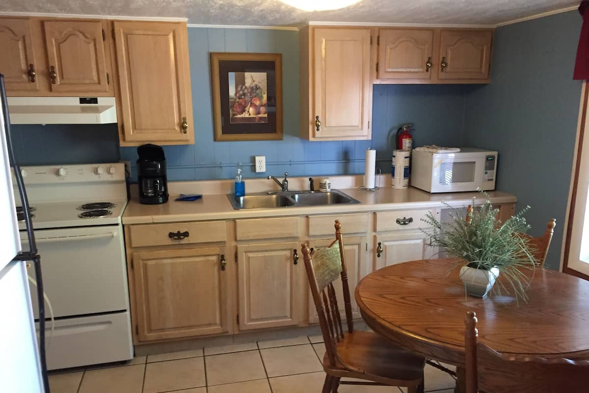 A kitchen with wooden cabinets, a stove, a sink, and a dining table with chairs.