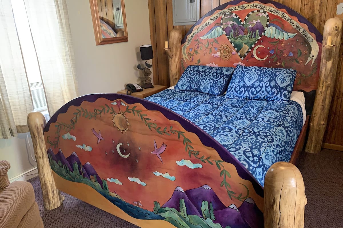 A bed with a colorful headboard and patterned bedding in a room with wooden walls and a mirror.