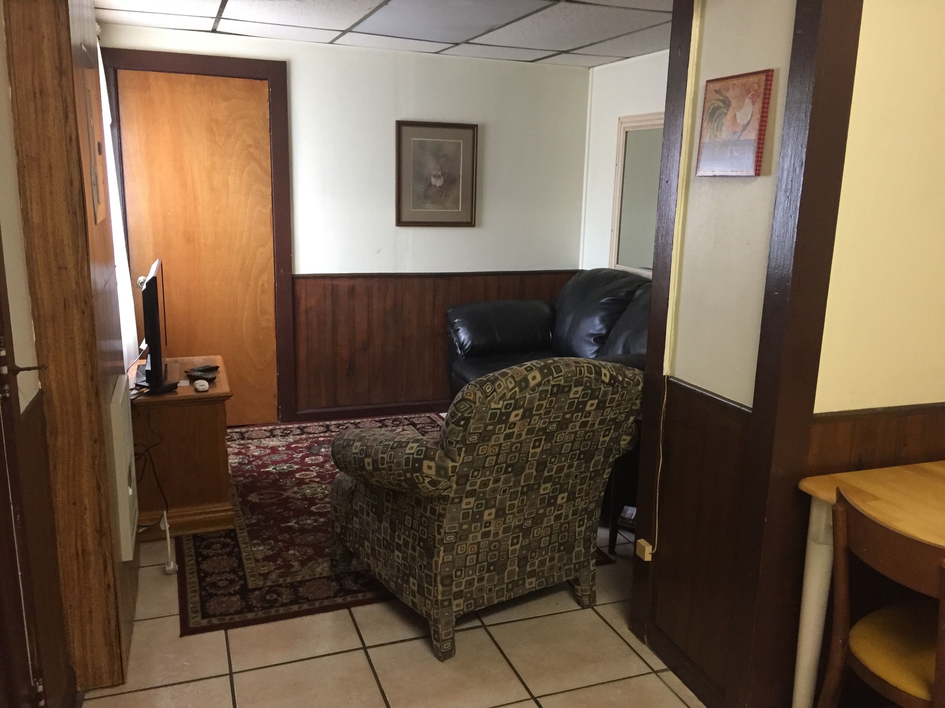 A room with a patterned armchair, a leather sofa, a wooden cabinet, and a framed picture on the wall.