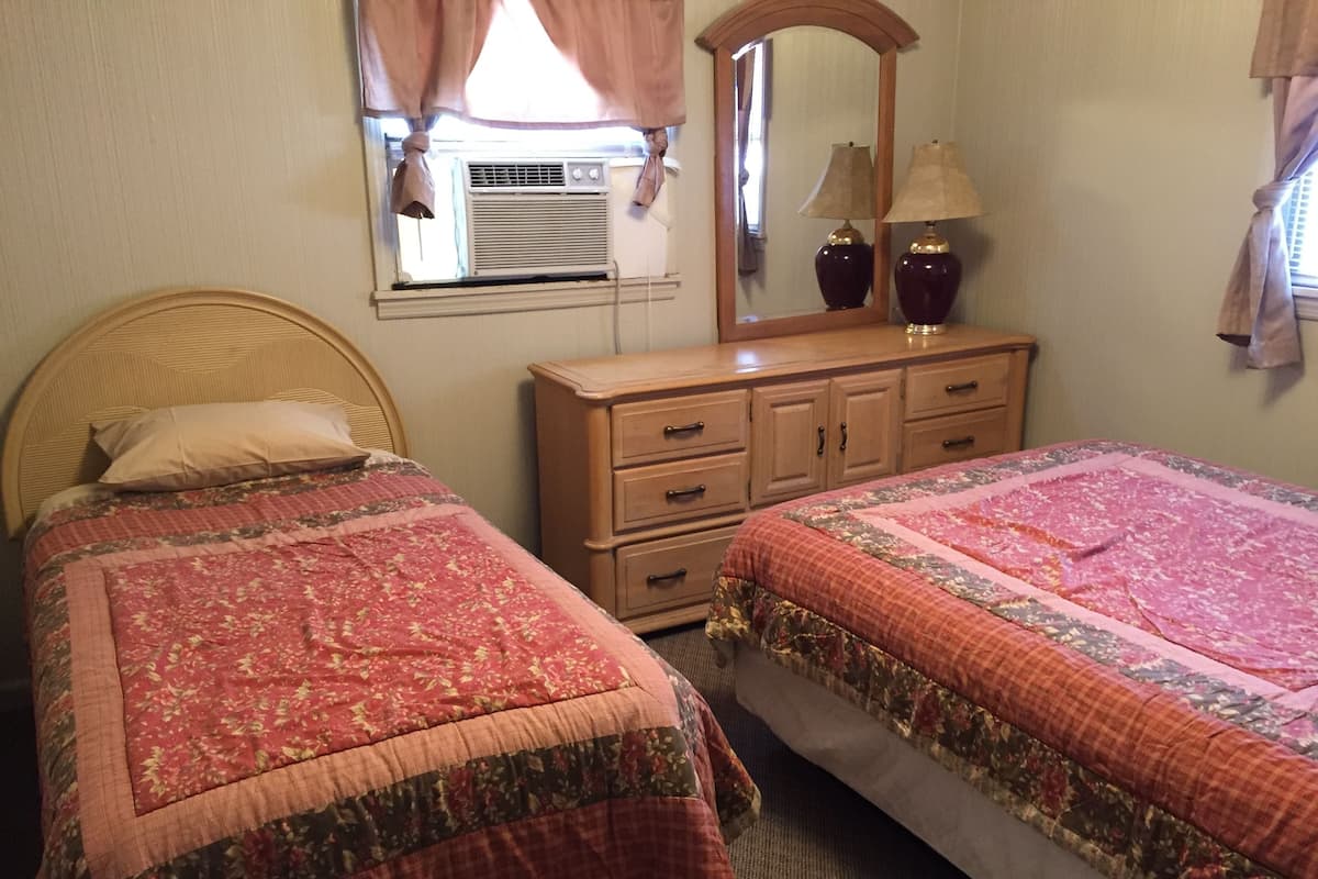 A bedroom with two beds, a dresser, a mirror, and a window with curtains.