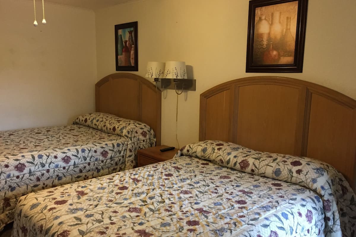 A room with two beds, each with floral bedding, a bedside table with a lamp, and framed artwork on the walls.