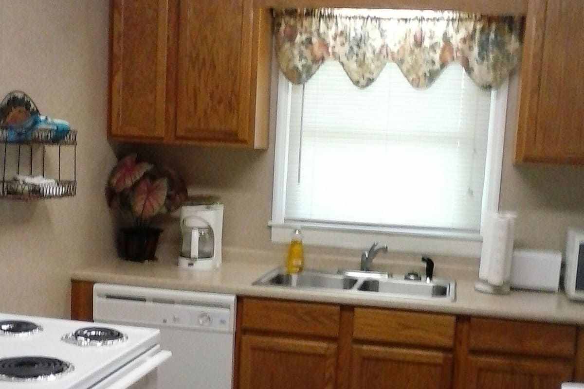 A kitchen with wooden cabinets, a stove, a dishwasher, a sink, and a window with a floral curtain.