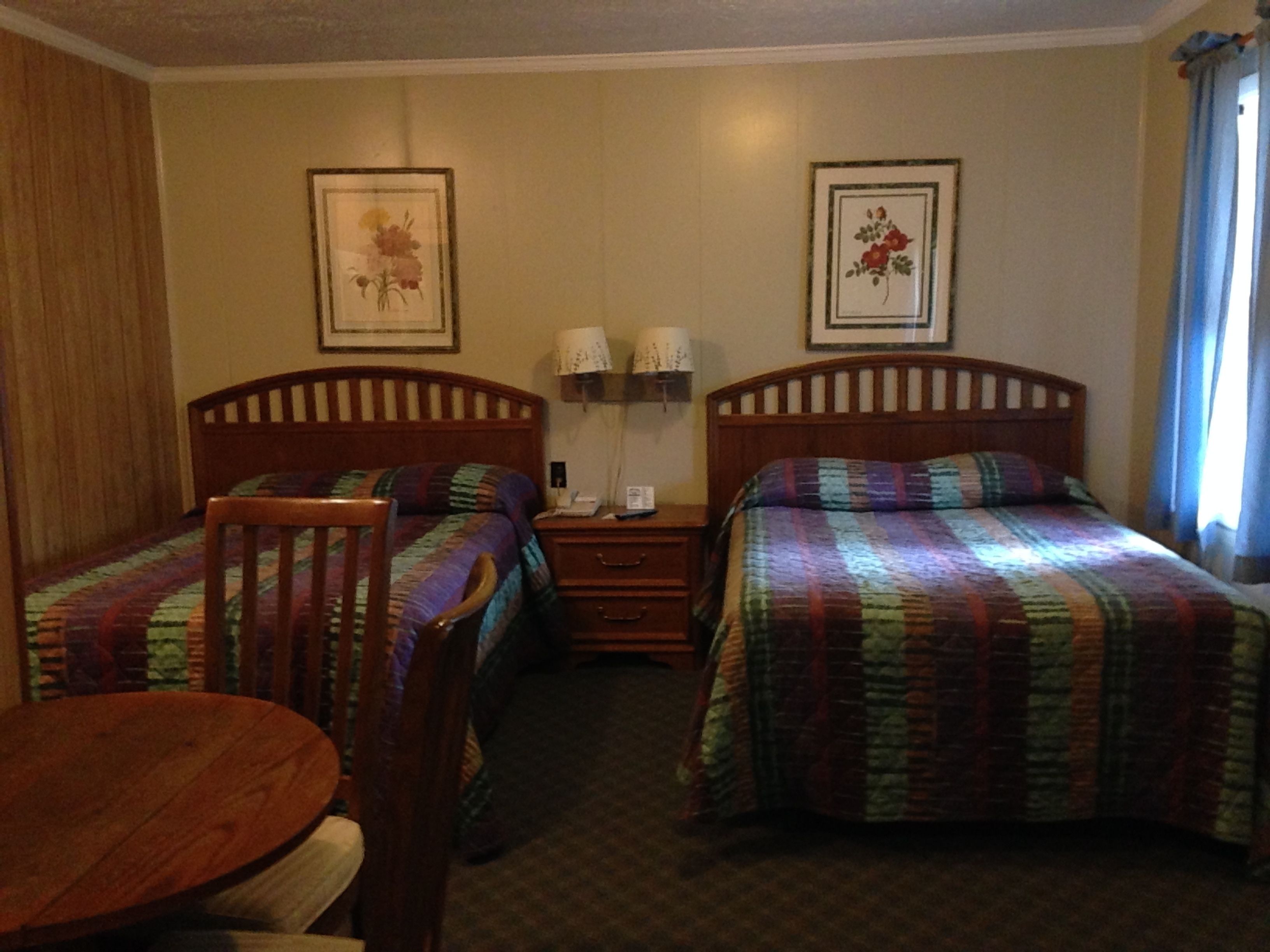 Une chambre d’hôtel avec deux lits simples, une chaise en bois, une petite table et une table de chevet avec une lampe.