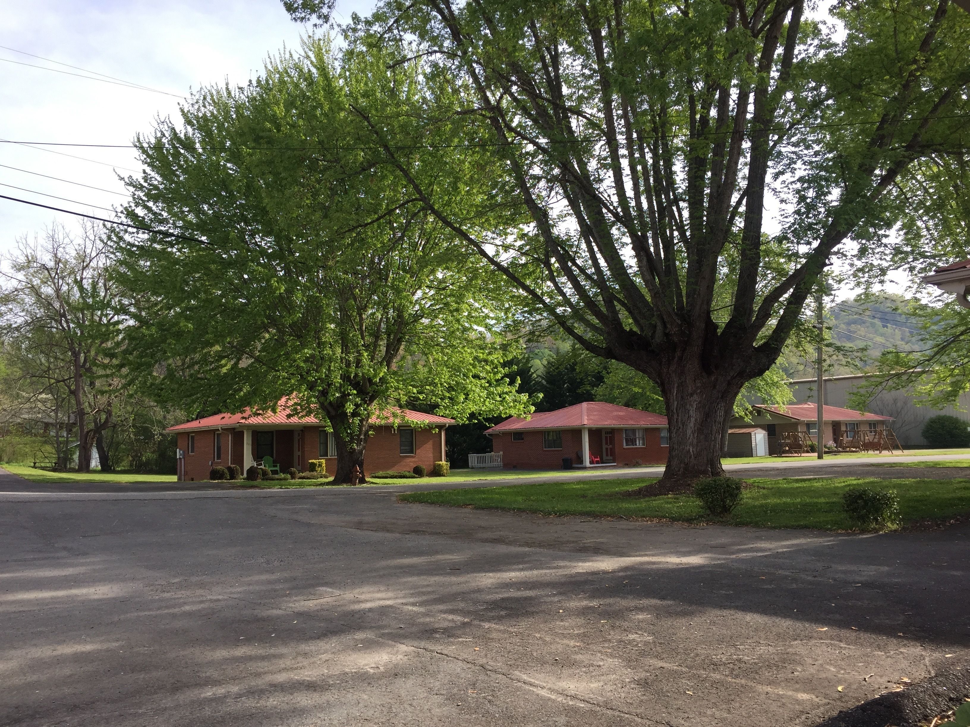 A residential area with two brick houses, each with a red roof, surrounded by lush green trees and a clear sky.
