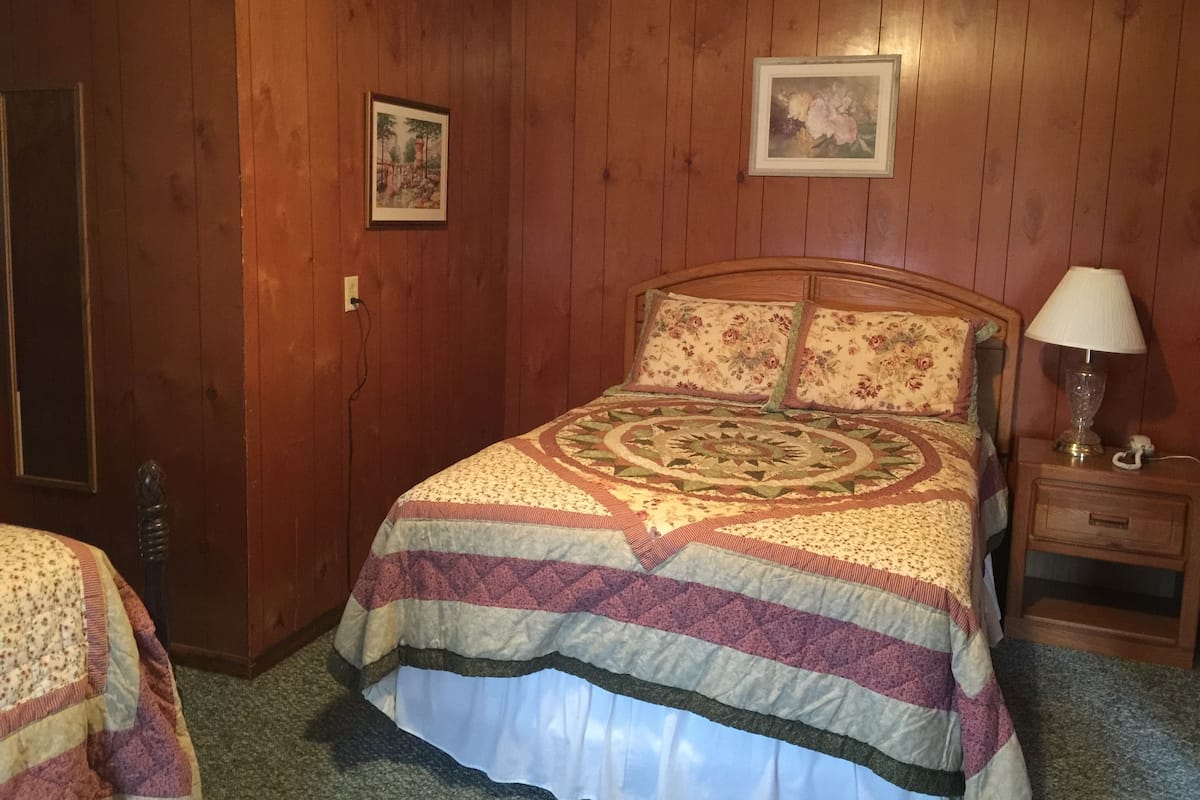 A wooden-paneled room with a bed, a nightstand, and a lamp.