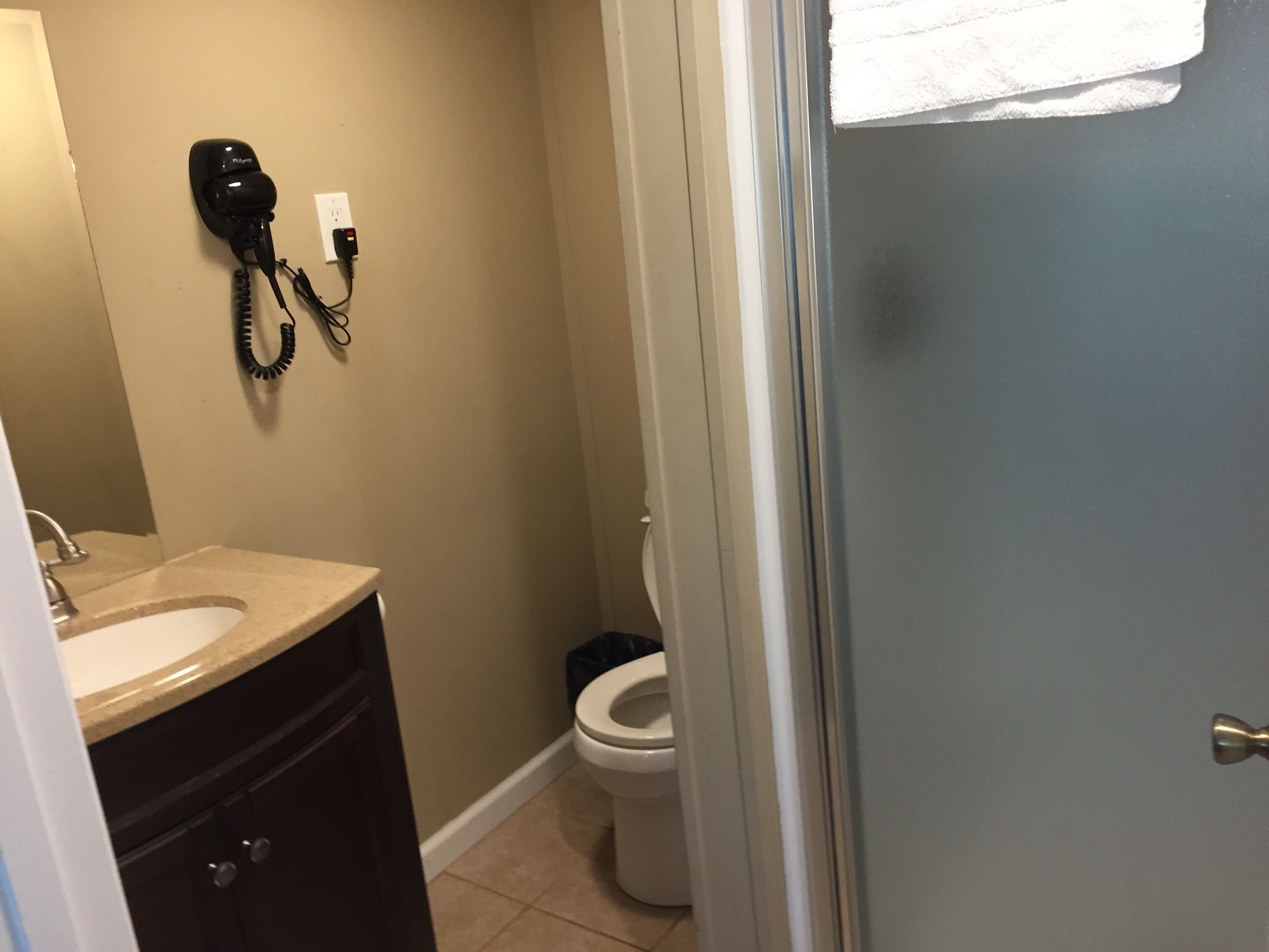 A bathroom with a sink, mirror, and toilet. A hairdryer is mounted on the wall.