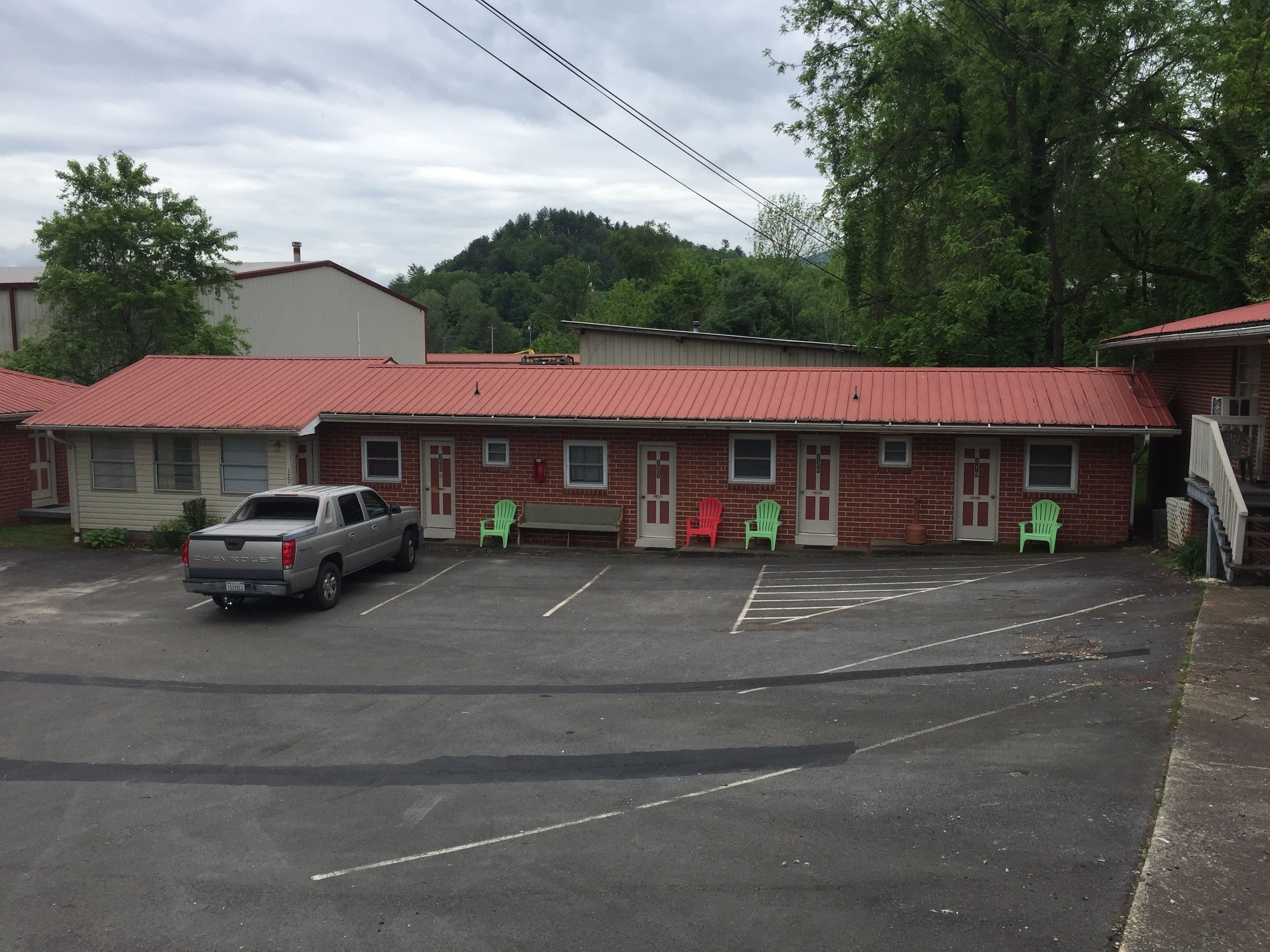 A motel with a red roof, a parking lot, and several green chairs outside.