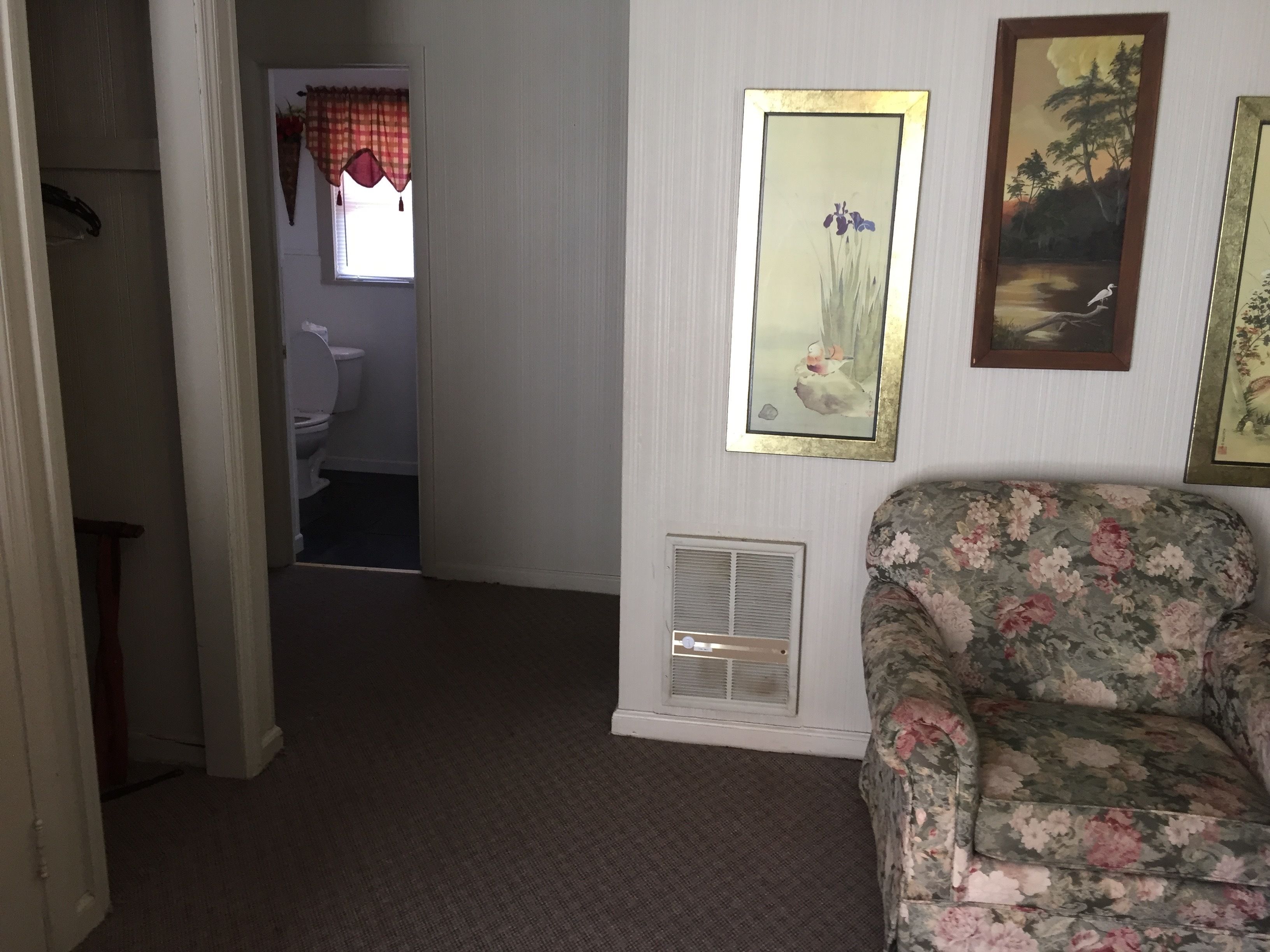 A room with a floral sofa, a window with a checkered curtain, and a painting on the wall.