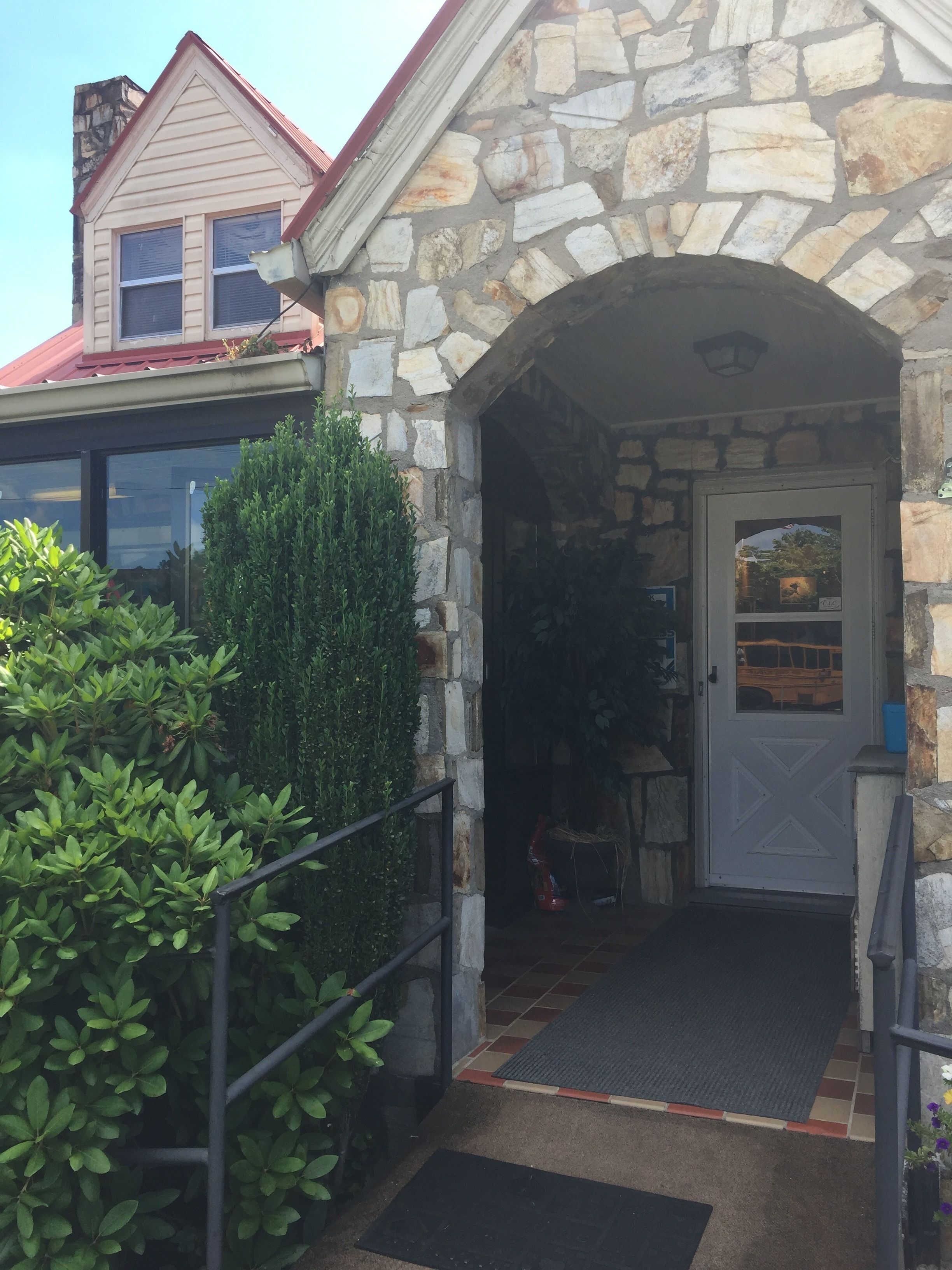 A stone building entrance with a door, a small porch area, and a metal railing.