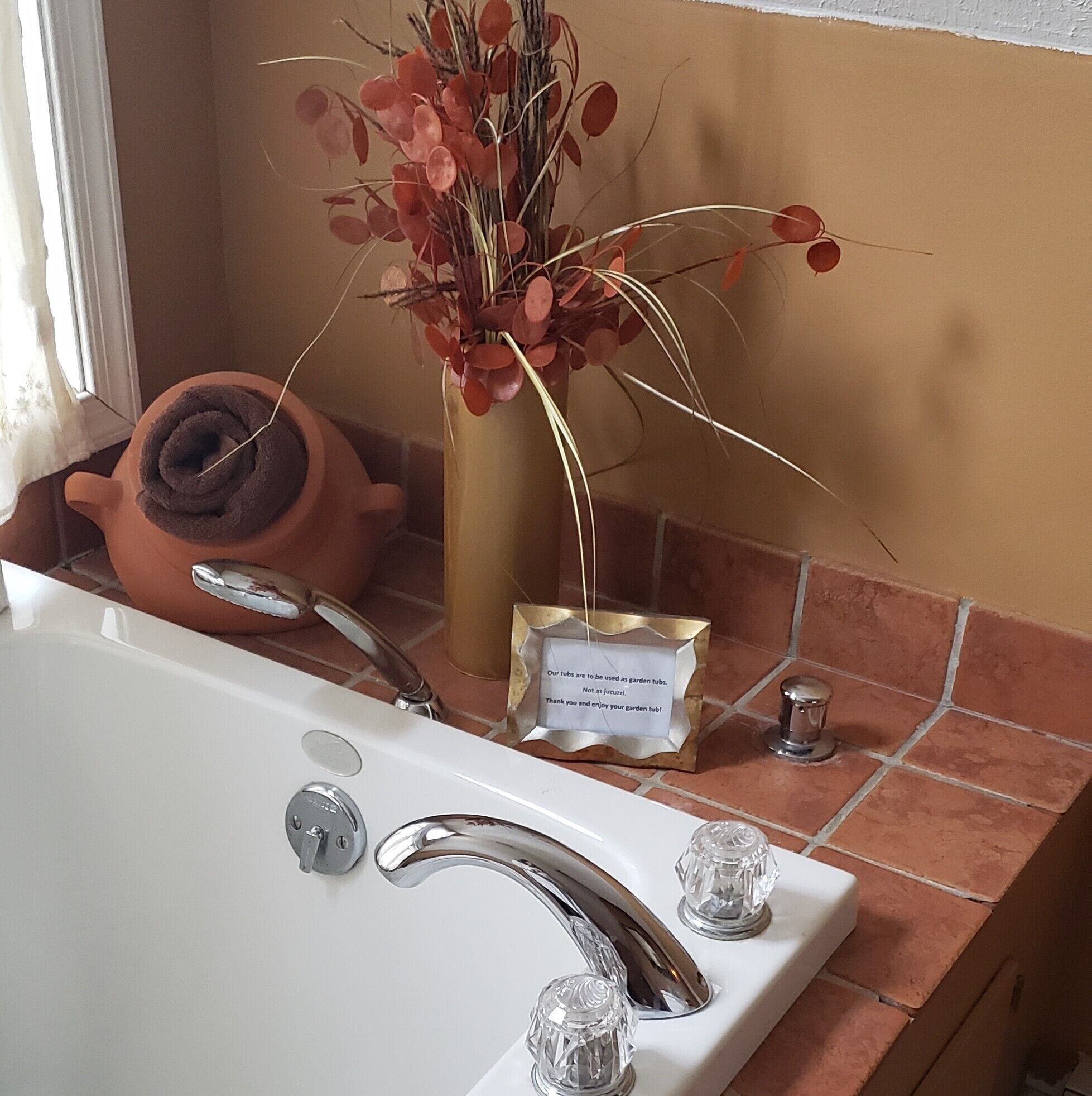 A bathroom with a white bathtub, a silver faucet, a terracotta pot, and a vase with red leaves.