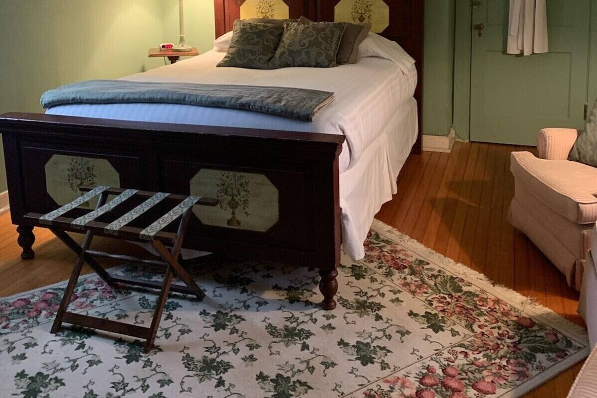 A bedroom with a wooden bed, a nightstand, a lamp, a robe hanging on the door, and a floral rug.