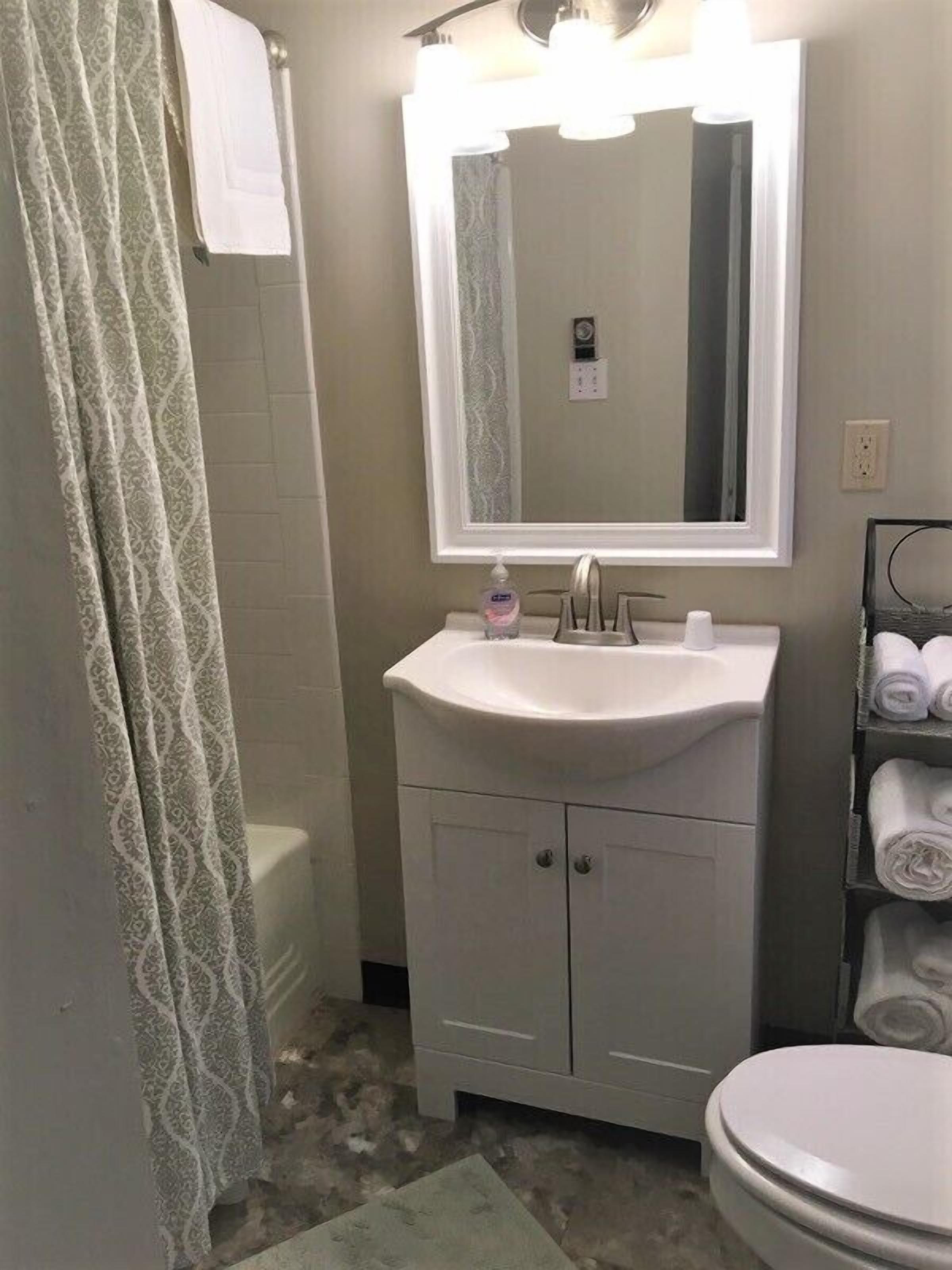 A bathroom with a white sink, a mirror, a toilet, and a towel rack with towels.