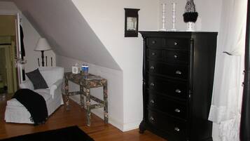 Une chambre à coucher avec un lit blanc, une commode noire, une petite table avec une lampe et une chaise.