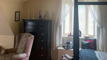 A bedroom with a bed, a dresser, a chair, a window with curtains, and a small table with items on it.