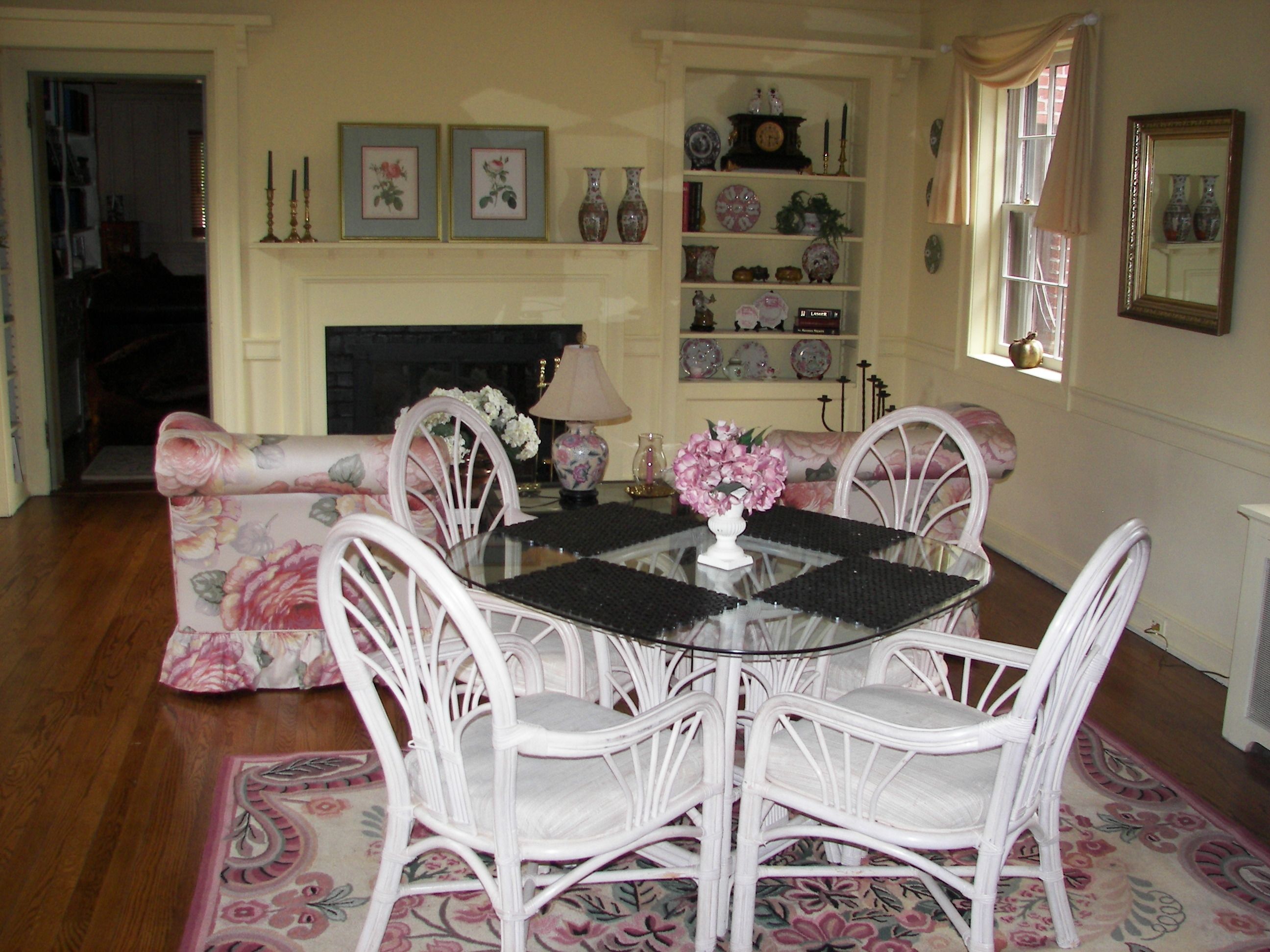 A dining area with a round table, white chairs, and a floral sofa.