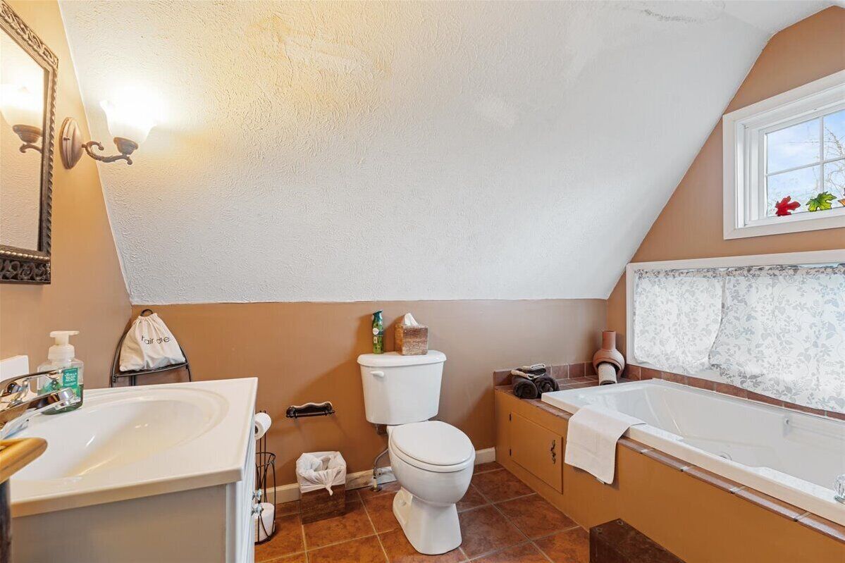 A bathroom with a toilet, sink, bathtub, and a window with lace curtains.