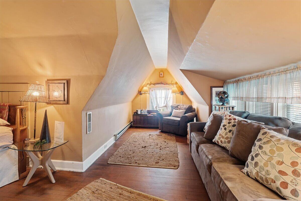 Un accogliente loft con soffitto spiovente, un'area salotto con divano e poltrone, un tavolino da caffè in vetro e un piccolo tavolino laterale.