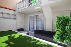A modern outdoor living area with a black sofa, a small table, and a green artificial lawn. - Aquarius Boutique Hotel (Rethymno)