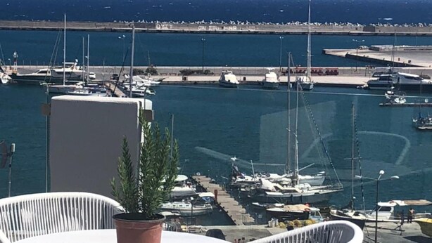 A terrace with a round table and two white chairs, overlooking a marina with boats and a clear view of the sea. - Aquarius Boutique Hotel (Rethymno)