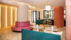 A modern lounge area with a teal sofa, a pink sofa, and a round table with chairs. - Aquarius Boutique Hotel (Rethymno)