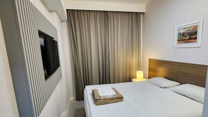 Habitación de hotel con cama, televisión montada en la pared, ventana con cortinas, un cuadro en la pared y una lámpara en el techo.