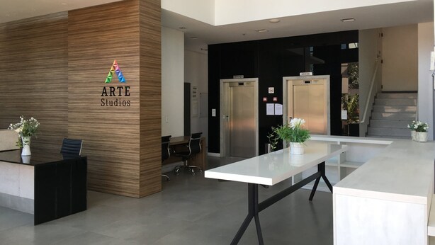 Un espacio de oficina moderno con un mostrador de recepción, dos puertas de acceso y servicio, una escalera y un diseño limpio y minimalista.