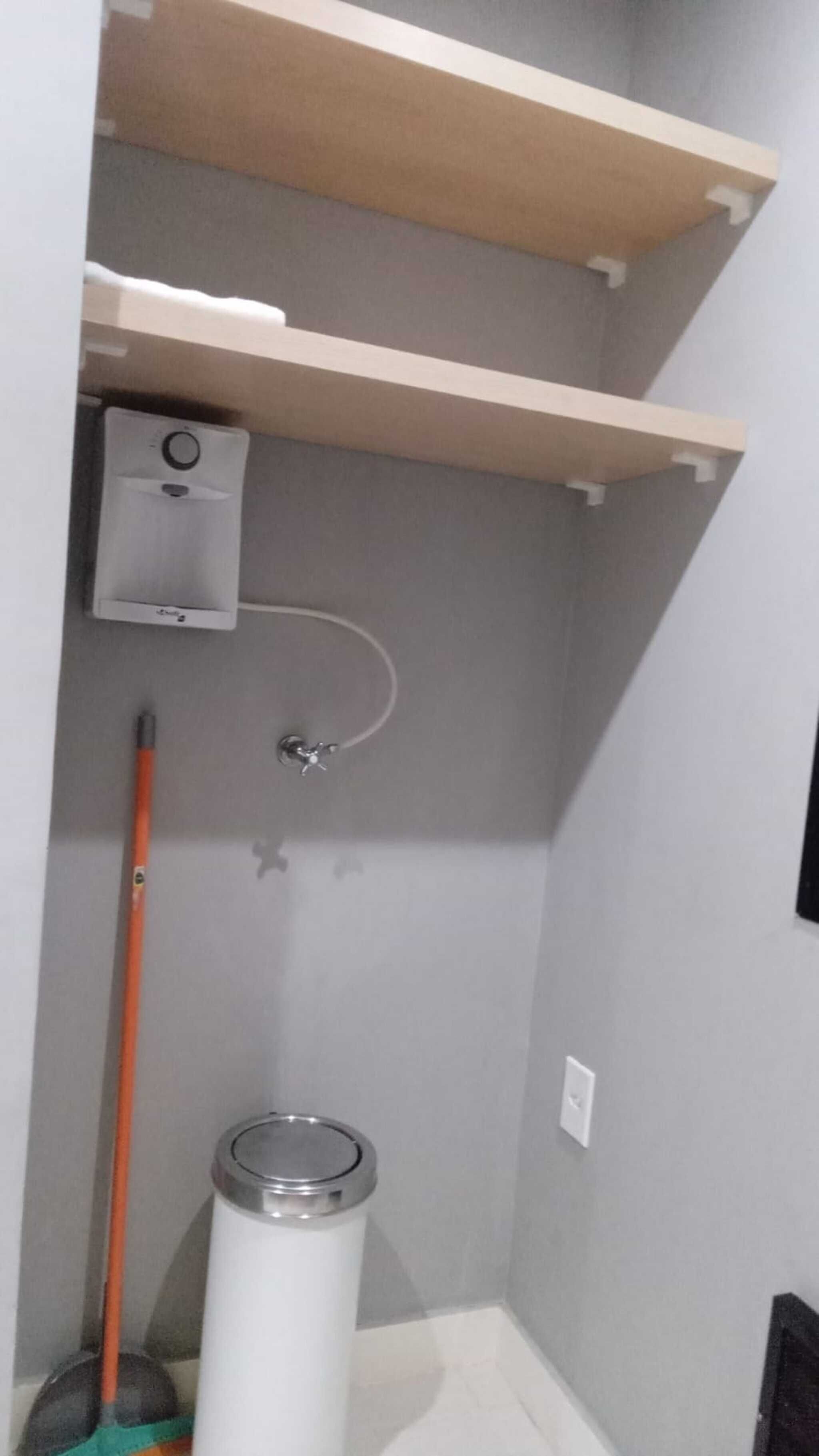 A corner of a room with a white trash bin, a broom, and a small white appliance on the wall.