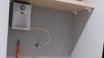 A corner of a room with a white trash bin, a broom, and a small white appliance on the wall.