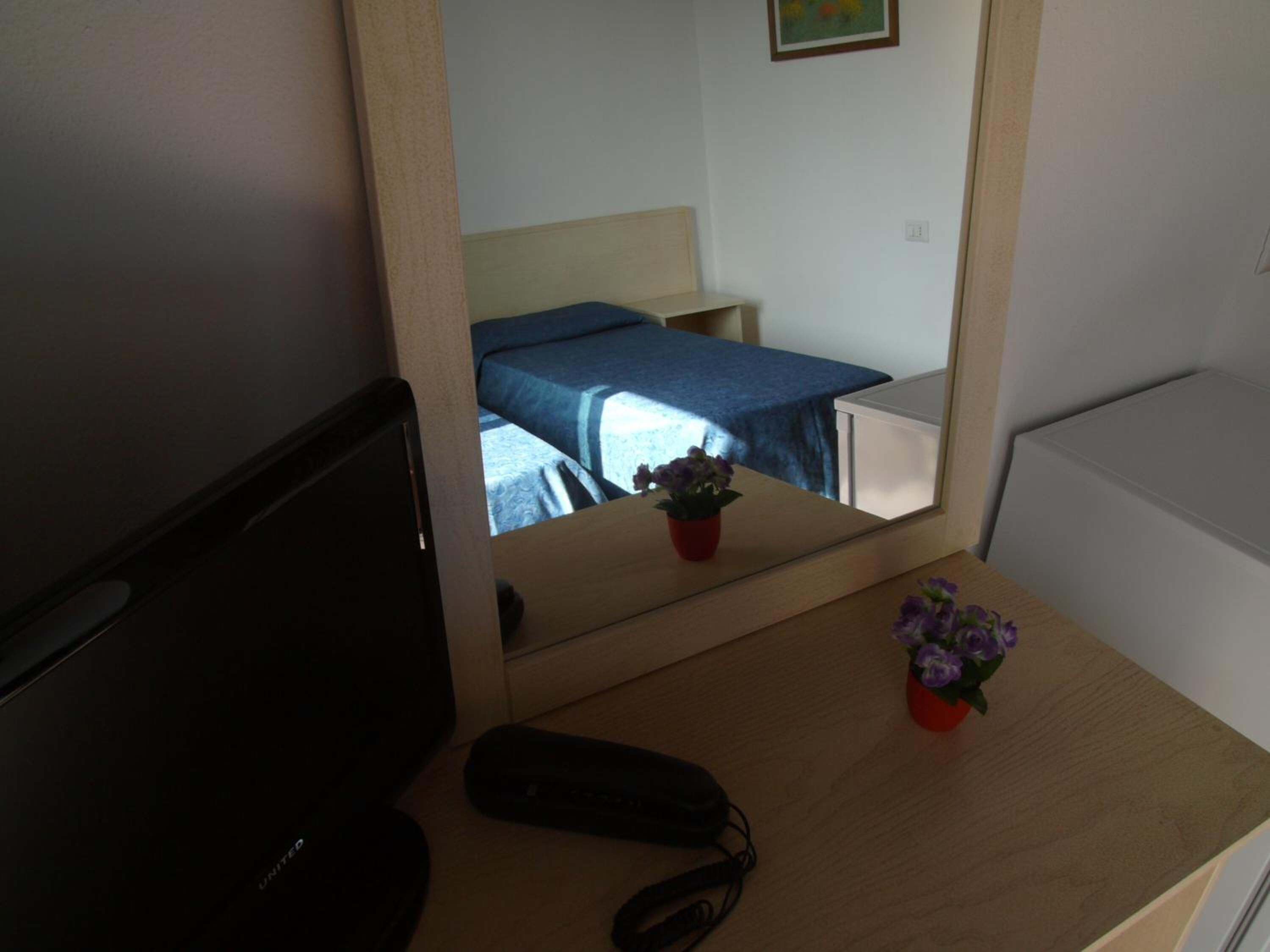 A hotel room with a bed, a small table with a potted plant, and a desk with a remote control.