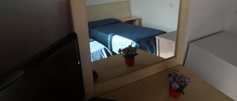 A hotel room with a bed, a small table with a potted plant, and a desk with a remote control.