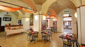 A dining area with brick arches, tables with chairs, and a buffet table with food. - Ostello Cagliari (Cagliari)