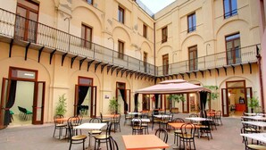 Une cour avec des espaces de repos en plein air, plusieurs tables et chaises, et un parasol central.