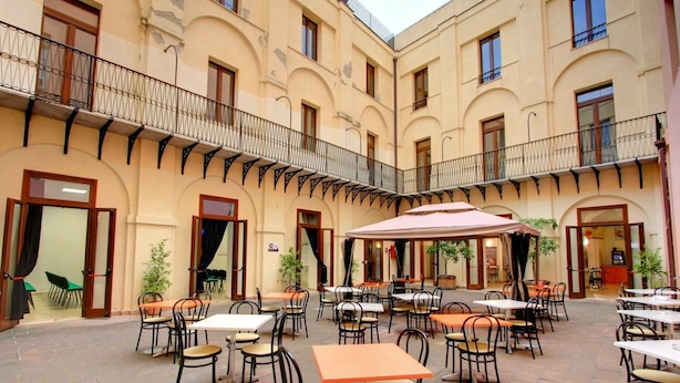 A courtyard with outdoor seating, multiple tables and chairs, and a central umbrella. - Ostello Cagliari (Cagliari)