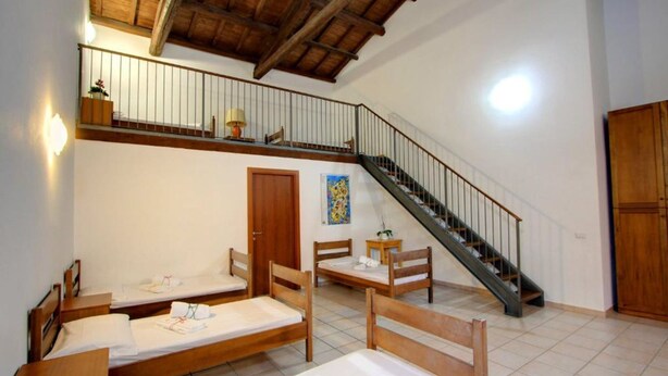 Une chambre de type dortoir, avec des lits en bois, un escalier et un balcon doté d’une balustrade.