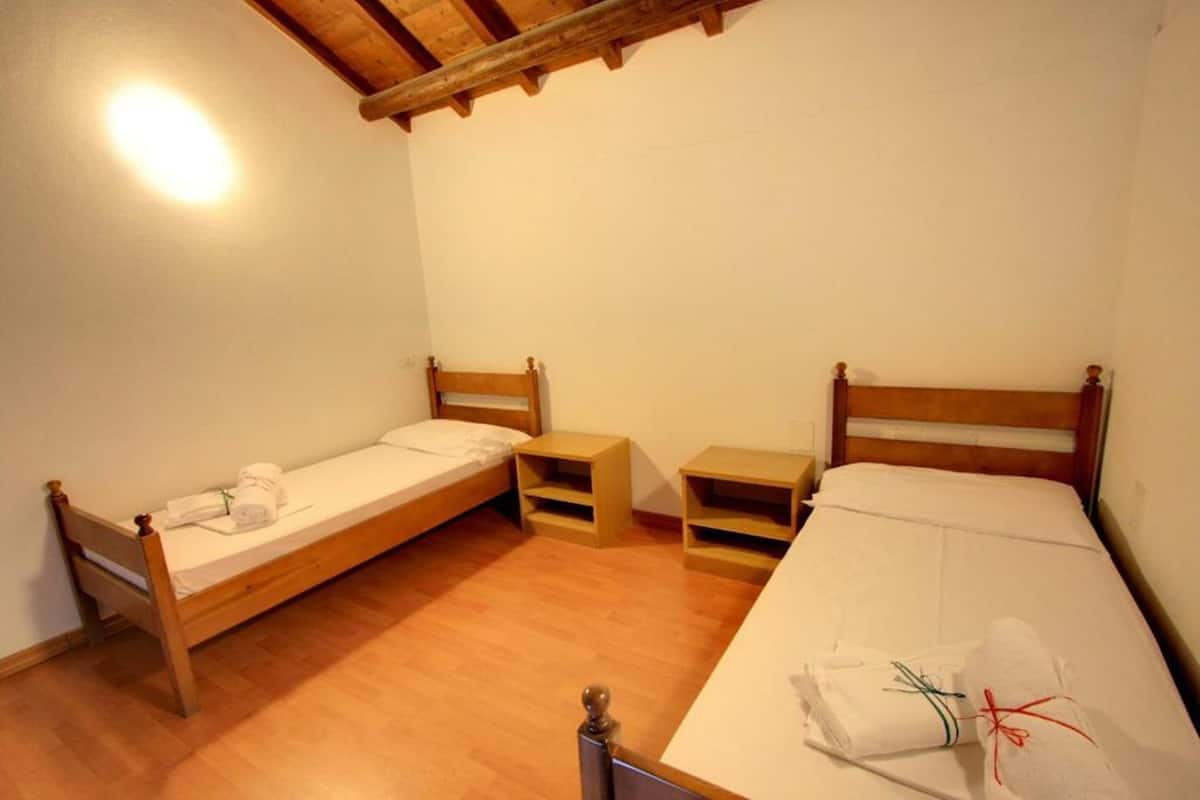 Un petit logement composé d’une seule pièce, avec deux lits en bois, chacun muni d’une table de chevet.