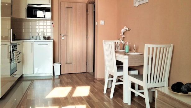 A compact kitchen with modern appliances, a dining area with a wooden table and chairs, and a door leading to another room.