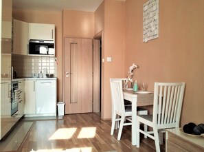 A compact kitchen with modern appliances, a dining area with a wooden table and chairs, and a door leading to another room. - Anděl Apartments (Prague)