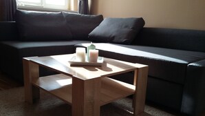 A small wooden table with candles and a tray, placed in front of a dark-colored sofa in a room with a carpeted floor.